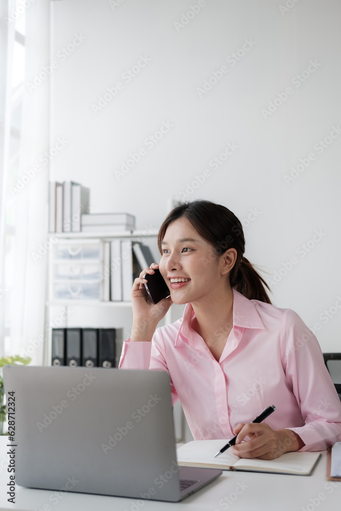 Young charming Asian businesswoman having a phone call with her client while working in the office room. Young charming Asian businesswoman having a phone call with her client while working in the office room.