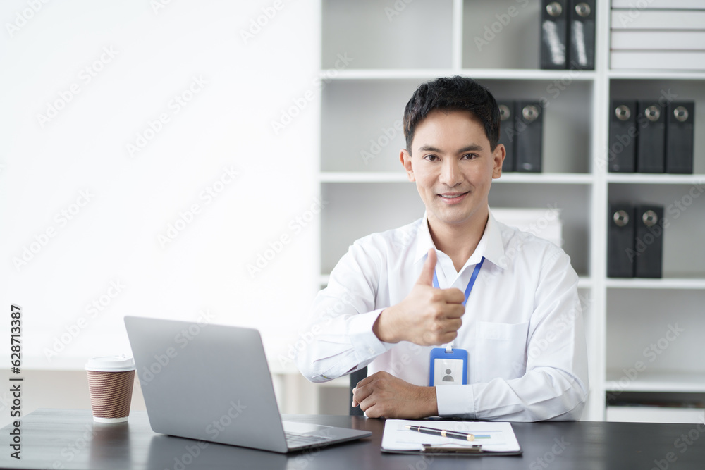 Smiling young Asian businessman working on his laptop and showing thumbs up. Smiling young Asian businessman working on his laptop and showing thumbs up.