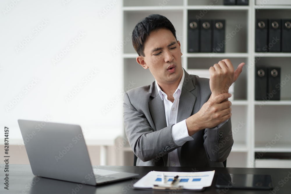 Young Asian businessperson touching his aching wrist with pained expression.