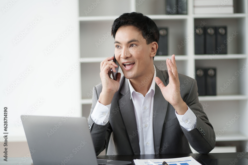 Young Asian businessman having a phone call with his client while sitting in the office room. Young Asian businessman having a phone call with his client while sitting in the office room.