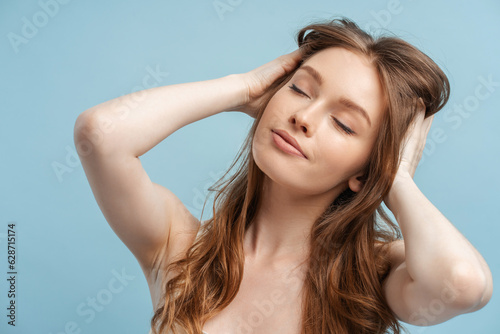 Attractive smiling woman touching her hair, taking shower isolated on blue background. Beautiful sexy fashion model with hairstyle posing for pictures with eyes closed. Hair care concept