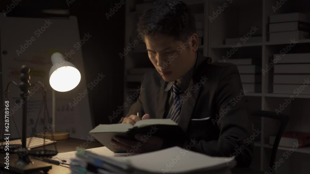 Smart and professional Asian male lawyer in formal suit sitting at desk at night in office. Lawyer, legal advisor. Smart and professional Asian male lawyer in formal suit sitting at desk at night in office. Lawyer, legal advisor.