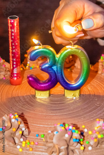 Happy 30th Candles shaped as the number 30 are coloured like a rainbow on top of a chocolate cake