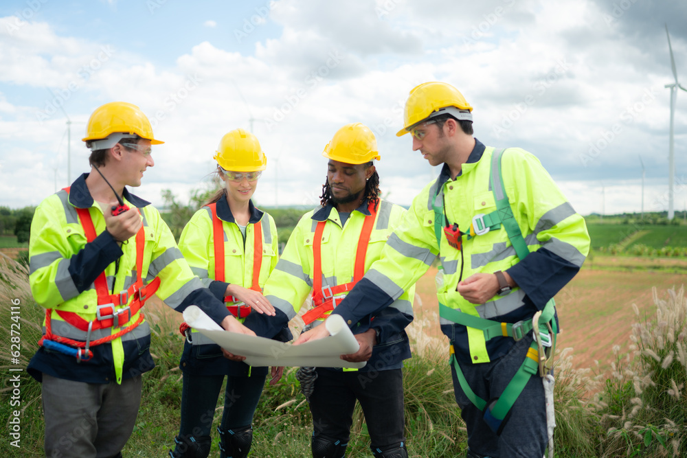 Group of engineers and technicians are discussing and looking at blueprints with wind turbines in the background Group of engineers and technicians are discussing and looking at blueprints with wind turbines in the background