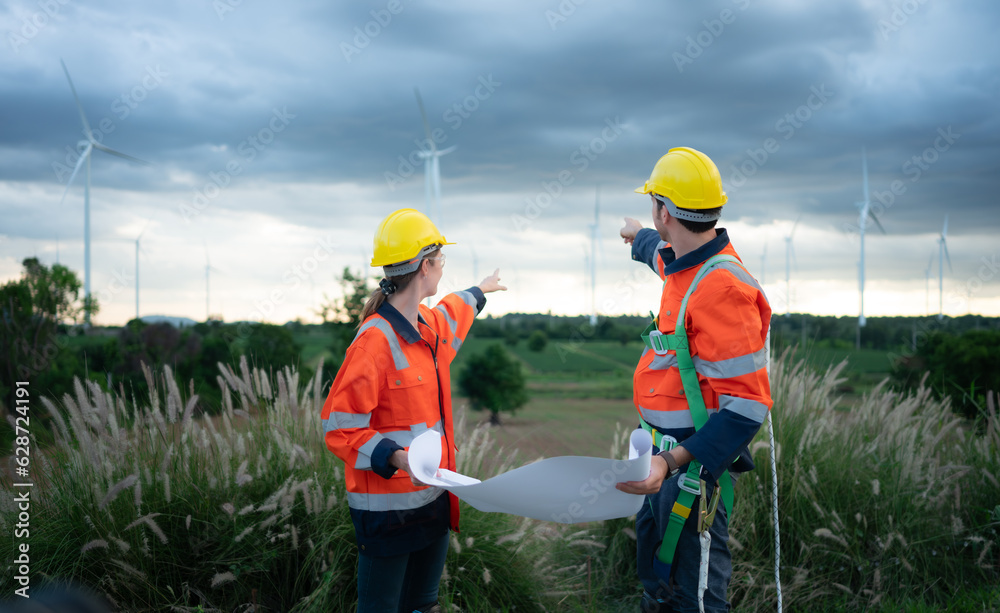 Two engineers working on a construction site with wind turbines in the background Two engineers working on a construction site with wind turbines in the background