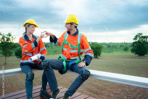 Two engineers discussing a project of wind turbine, They are sitting on a wooden platform, The concept of natural energy from wind. © Wosunan