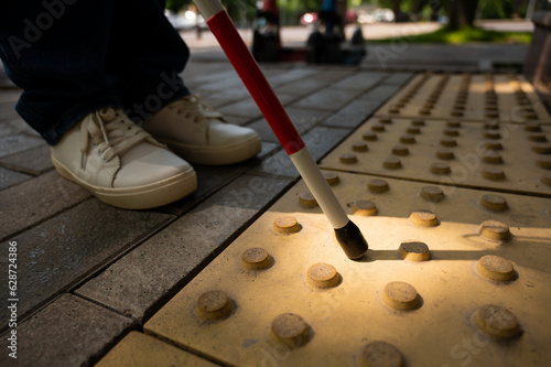 A close-up of a woman's feet with a tactile cane and a tactile tile indicating an obstacle.