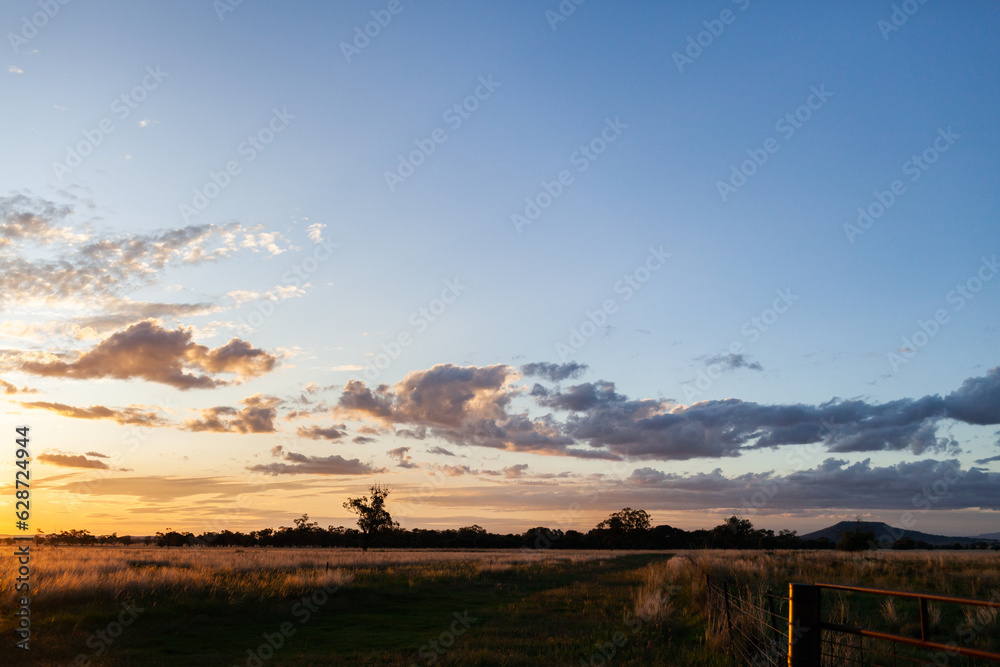 Sunset sky over grassy farmland with fence to the side Sunset sky over grassy farmland with fence to the side