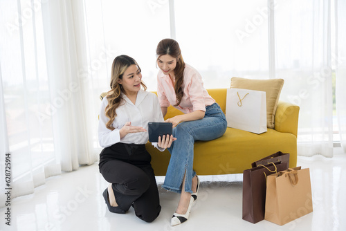 Modern Salesperson Using Digital Tablet to Pitch Product to Asian woman Customers sitting on the sofa in shopping mall- Interactive Marketing and Retail Display