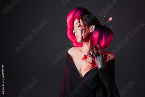 fighting geisha in a black kimono splashes blood on her face. Halloween image. young multiethnic woman in a bright Asian costume. voluminous hairstyle with scarlet hair and decorative hairpins
