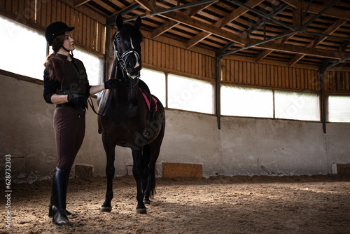 Equestrian sports. A young woman in a sports uniform, a rider and her horse in the arena, preparing for training with a dressage horse.
