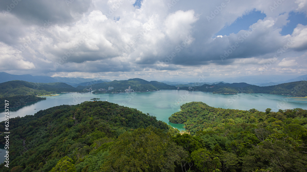 From Ci'en Pagoda, mesmerizing vista unfolds, panoramic view of Sun Moon Lake Taiwan, with surrounding mountain landscape. The tranquil lake mirrors the sky, while lush green peaks embrace its shores