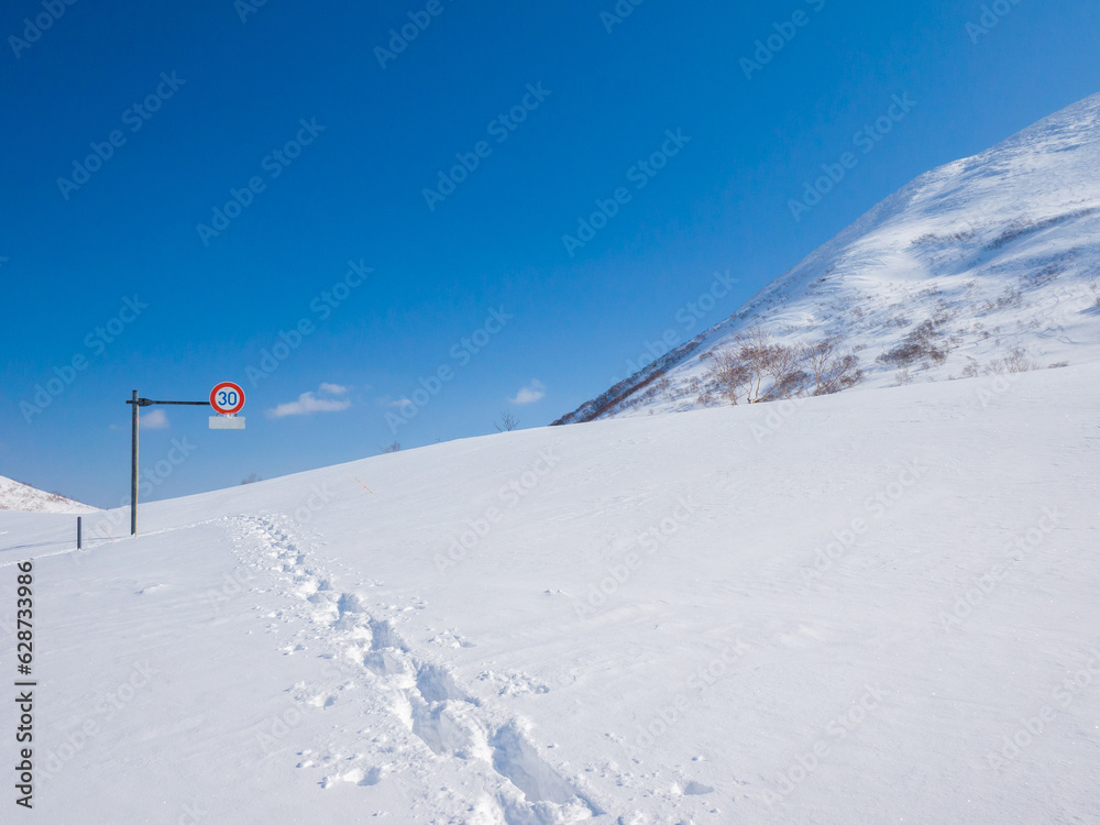 (Niseko, Hokkaido, Japan)Footprints towards a road sign half buried in deep snow (Niseko, Hokkaido, Japan)Footprints towards a road sign half buried in deep snow