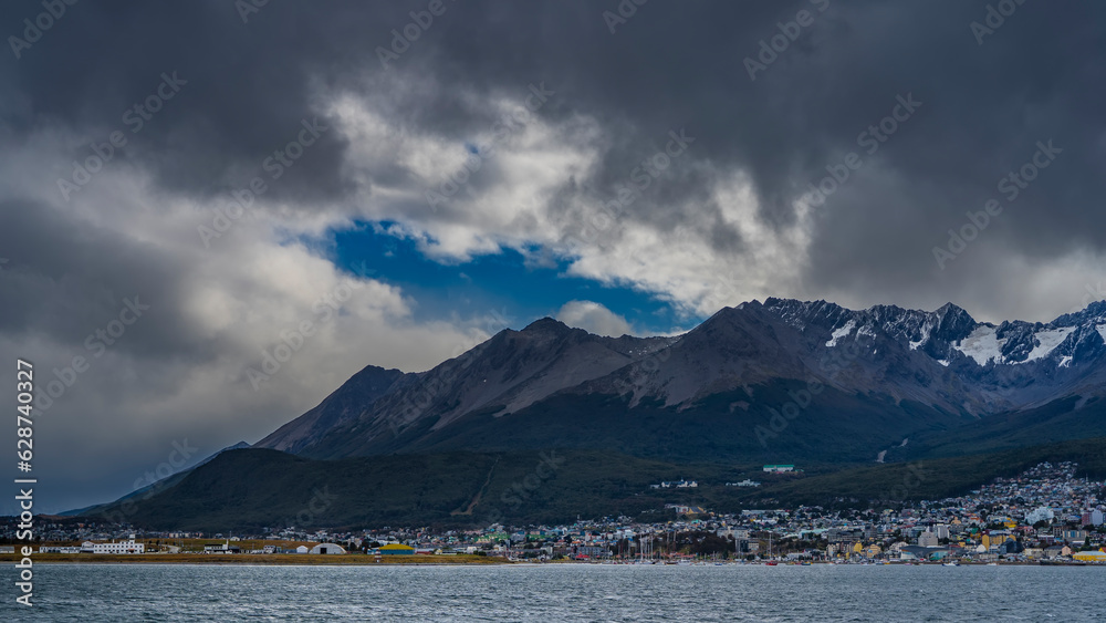 The picturesque mountain range of the Andes- Martial - against the sky and clouds. City houses are visible on the bank of the Beagle Canal. Argentina. Ushuaia. Tierra del Fuego Archipelago. The picturesque mountain range of the Andes- Martial - against the sky and clouds. City houses are visible on the bank of the Beagle Canal. Argentina. Ushuaia. Tierra del Fuego Archipelago.