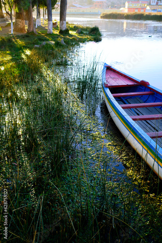 vertical photo of rustic boat on lake with trees and sun rays in summer in la paz bolivia hispanic america photo