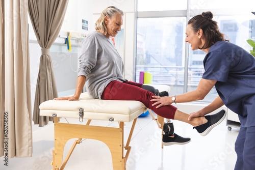 Caucasian female physiotherapist and senior woman with artificial leg stretching at hospital