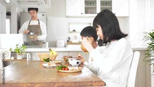 自宅で朝食を食べる子供と料理をしている男性