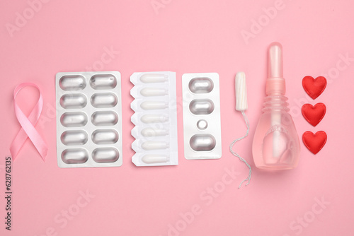 Women's health, treatment of women's diseases. Vaginal suppositories, pill blisters, tampon, pink awareness ribbon on pink background. Flat lay © splitov27