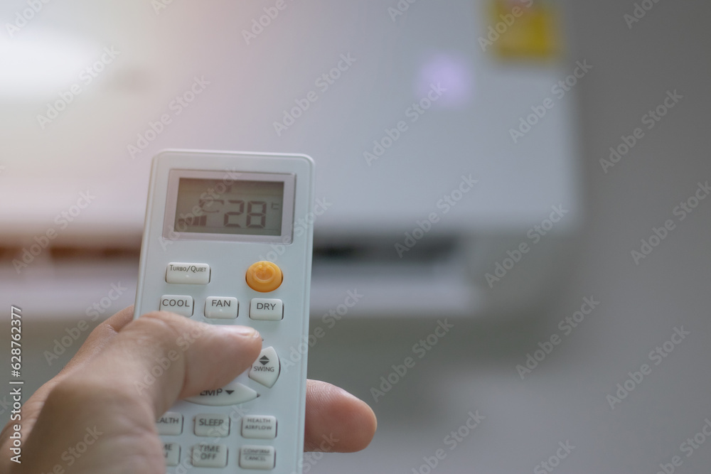 Close-up picture of adjusting the air conditioner temperature with a remote control in the room at home Close-up picture of adjusting the air conditioner temperature with a remote control in the room at home