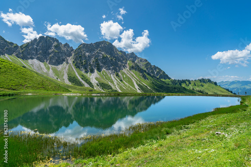 die Berge Breithorn und Kellaspitze spiegeln sich im Wasser des Speichersee der Oberpartnomalpe. Sommer mit Panorama im Grosswalsertal, Vorarlberg