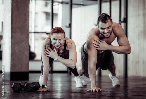 Athletic smiling couple man and woman do push-ups together in the gym. Healthy lifestyle