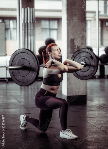 Athletic woman training lunges with heavy barbell in modern gym