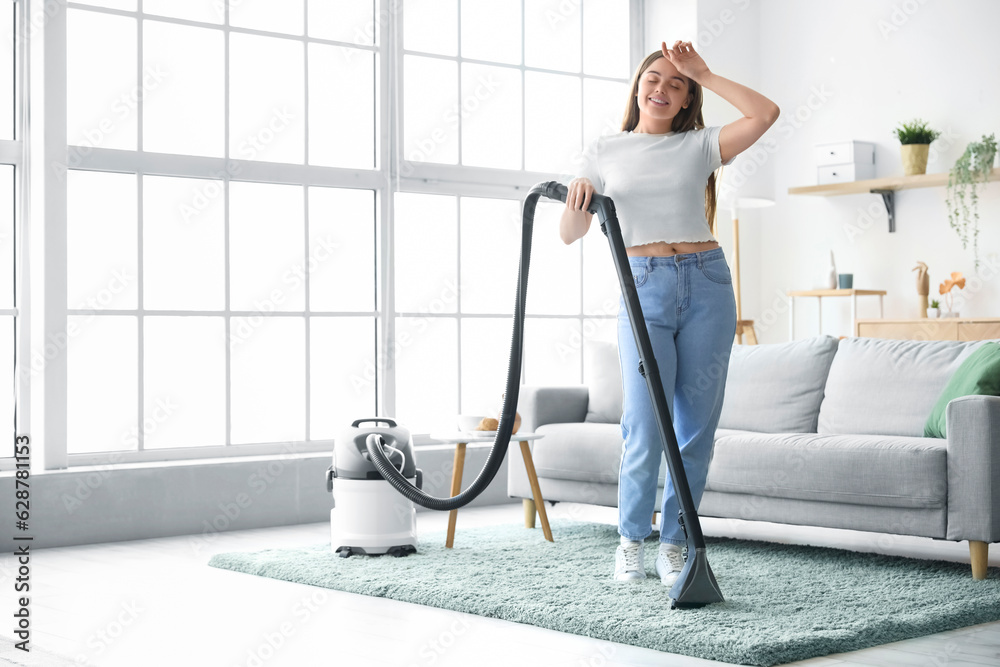 Fototapeta premium Tired young woman hoovering carpet at home