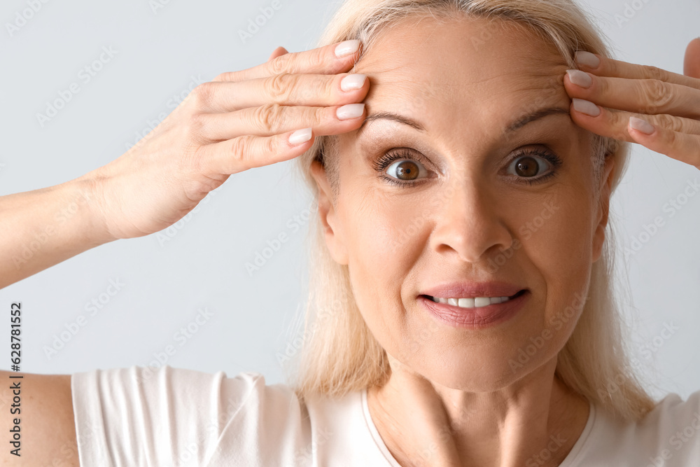 Mature woman doing face building exercise on light background, closeup Mature woman doing face building exercise on light background, closeup