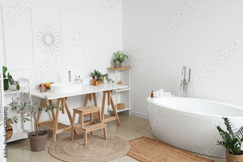 Interior of light bathroom with white sink, bathtub and houseplants © Pixel-Shot