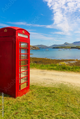 Portrait of a red, old fashioned telephone box overlooking yachts in the bay on the Isle of Canna, Small Isles, Scotland.  Copy Space, vertical. © Anne Coatesy
