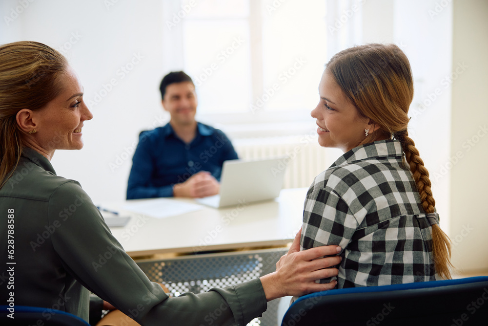 Happy teenage girl talks to her mother in principal's office at high school.