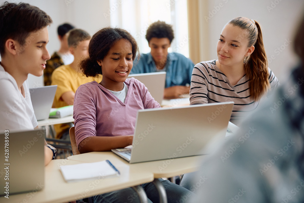 Happy high school students e-learning on computer during class in classroom.