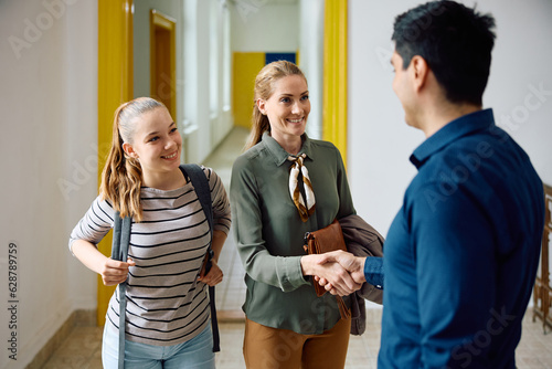 Happy mother of teenage girl shaking hands with high school principal in hallway. photo