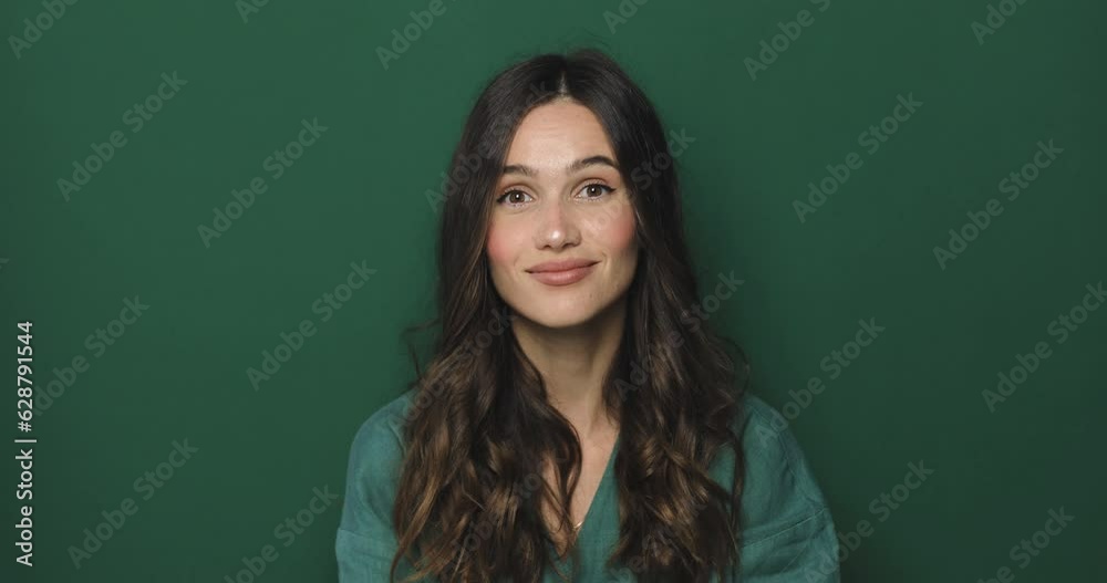 Smiling attractive brunette curly woman looking at camera listening to someone and nodding with agree standing over green studio background. Smiling attractive brunette curly woman looking at camera listening to someone and nodding with agree standing over green studio background.