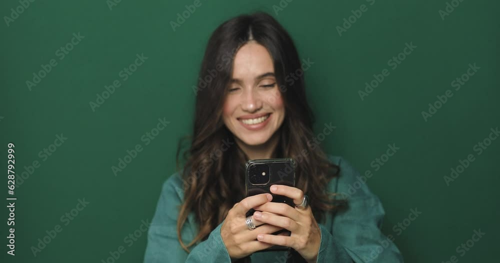 Great application or website. Excited woman using her mobile phone, isolated on green studio background. Positive lady holding gadget, looking at camera, texting, messaging. Focus on mobile phone. Great application or website. Excited woman using her mobile phone, isolated on green studio background. Positive lady holding gadget, looking at camera, texting, messaging. Focus on mobile phone.