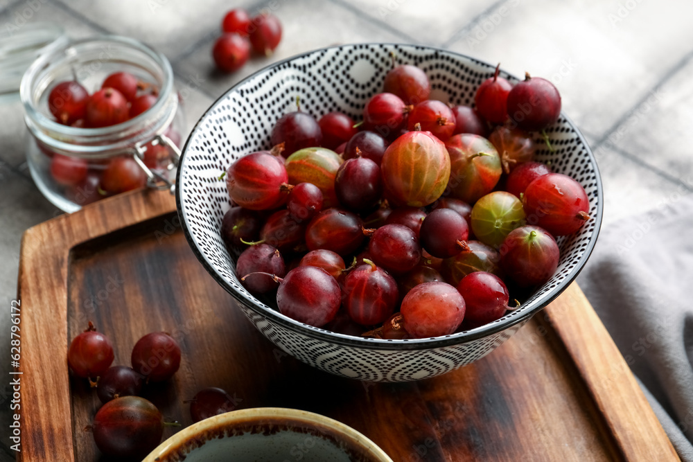 Bowl and jar with fresh gooseberries on grey tile background Bowl and jar with fresh gooseberries on grey tile background