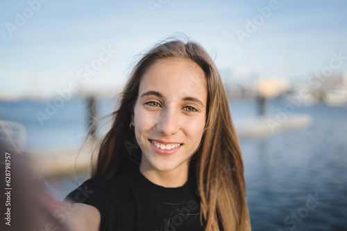 Happy Spanish teenager smiling in the harbor. Close-up Portrait of a happy young adult Hispanic woman in the harbor of a European city. Close-up of Spanish woman with perfect white teeth.