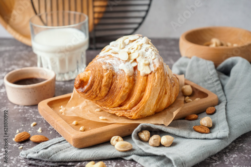 Wooden board of sweet croissant with powdered sugar and nuts on dark table