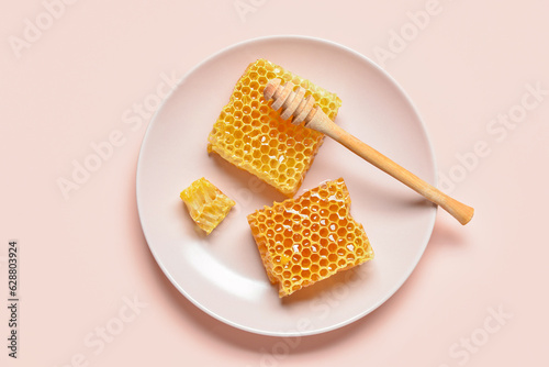 Plate with sweet honeycombs and dipper on pink background