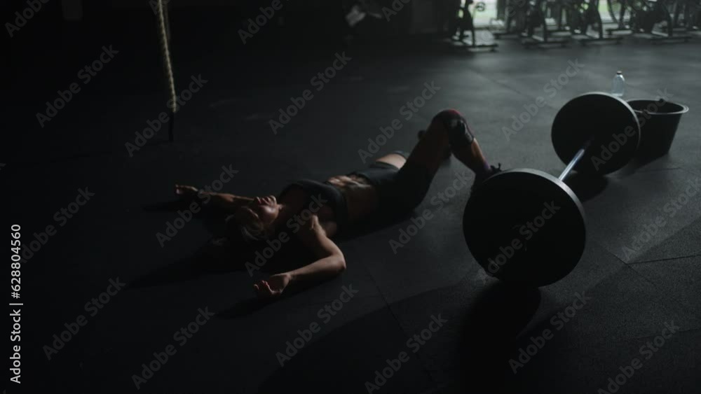 Exhausted Sportswoman Lying On Floor Near Barbell In Gym, Resting And Breathing Hard After Workout
