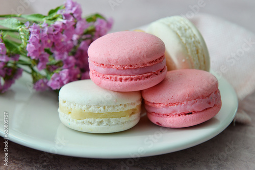 Foto Plate with sweet macaroons and beautiful flowers on pink background