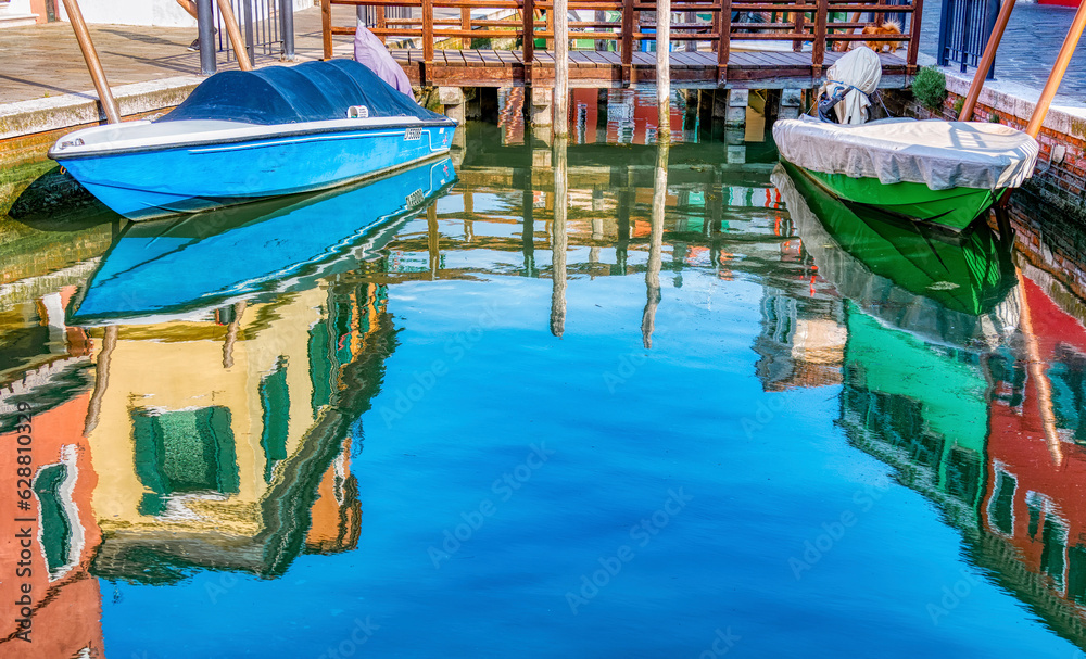 Picturesque colorful idyllic scene with a boat docked on the water canals in Burano Venice Italy. Water reflection.