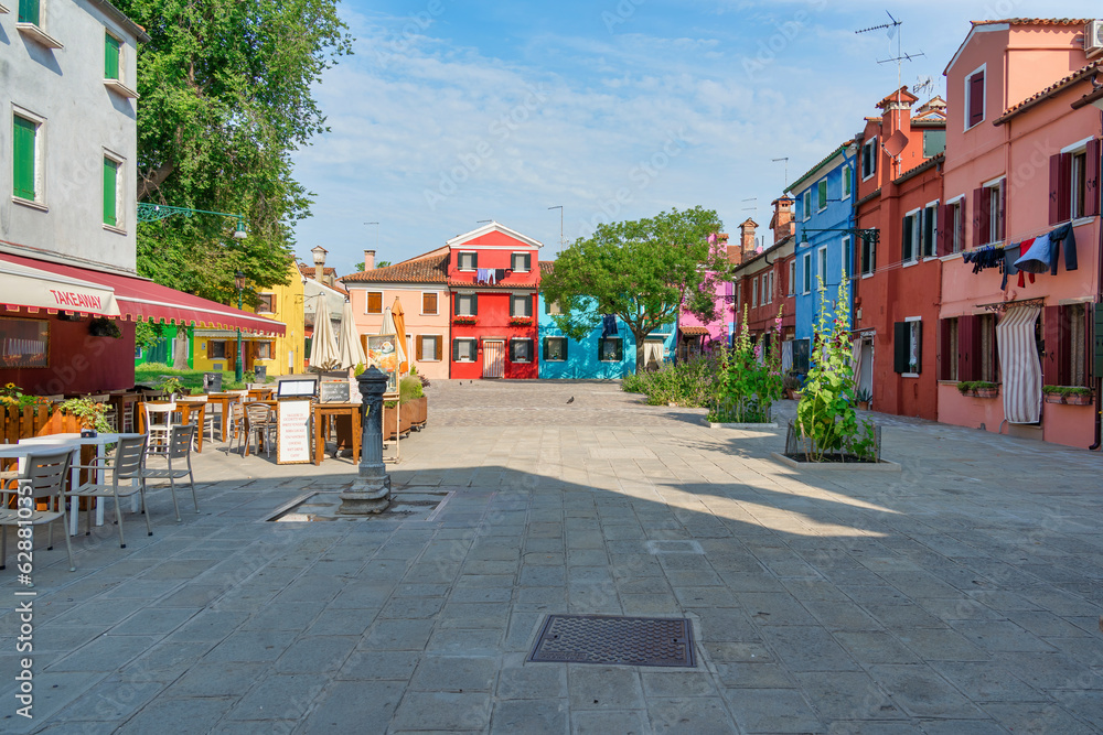 A small Piazzetta with outdoor restaurants cafes and colorful building in the island of Burano, Venice.