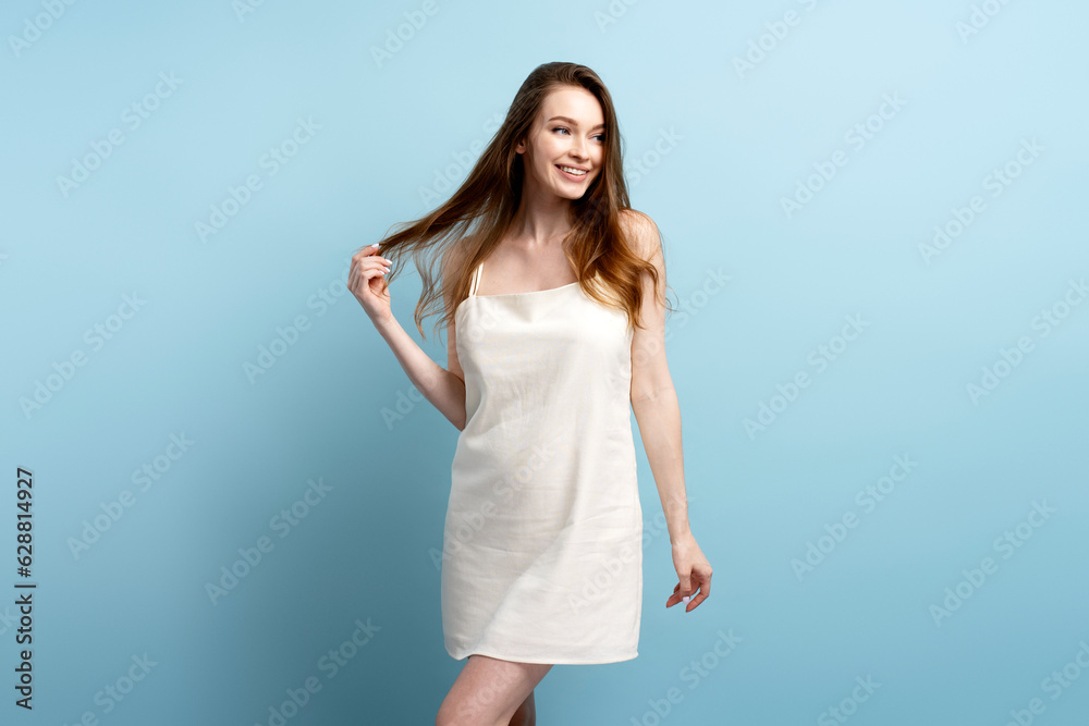 Attractive smiling woman with long hair wearing stylish elegant nightie, dress isolated on blue background. Beautiful sexy fashion fashion model posing for pictures in studio. Beauty concept Attractive smiling woman with long hair wearing stylish elegant nightie, dress isolated on blue background. Beautiful sexy fashion fashion model posing for pictures in studio. Beauty concept