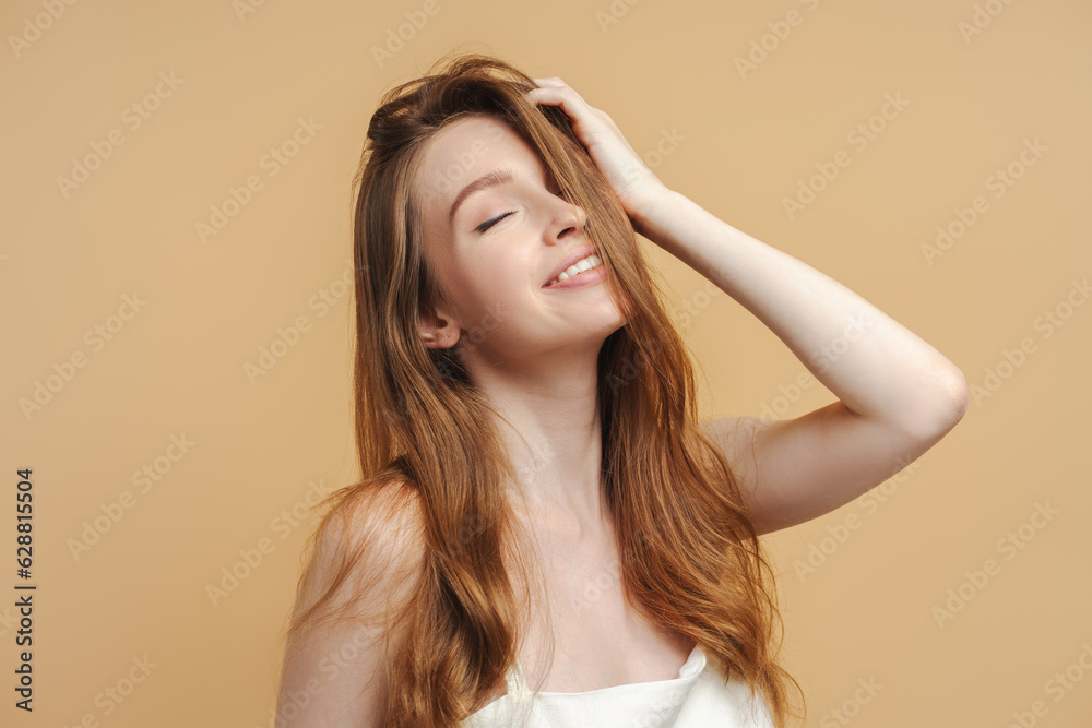 Beautiful smiling sexy woman wearing elegant nightie dress looking touching her hair isolated on beige background. Attractive fashion model posing for picture in studio. Beauty, hair care concept Beautiful smiling sexy woman wearing elegant nightie dress looking touching her hair isolated on beige background. Attractive fashion model posing for picture in studio. Beauty, hair care concept