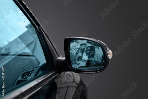 Black wing mirror of modern car. Car side rear-view mirror with water drops.