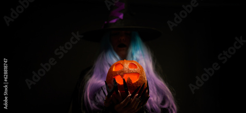 Witch with blue and violet hair, black hat with violet ribbon and long black nails is holding pumpkin in her hands.