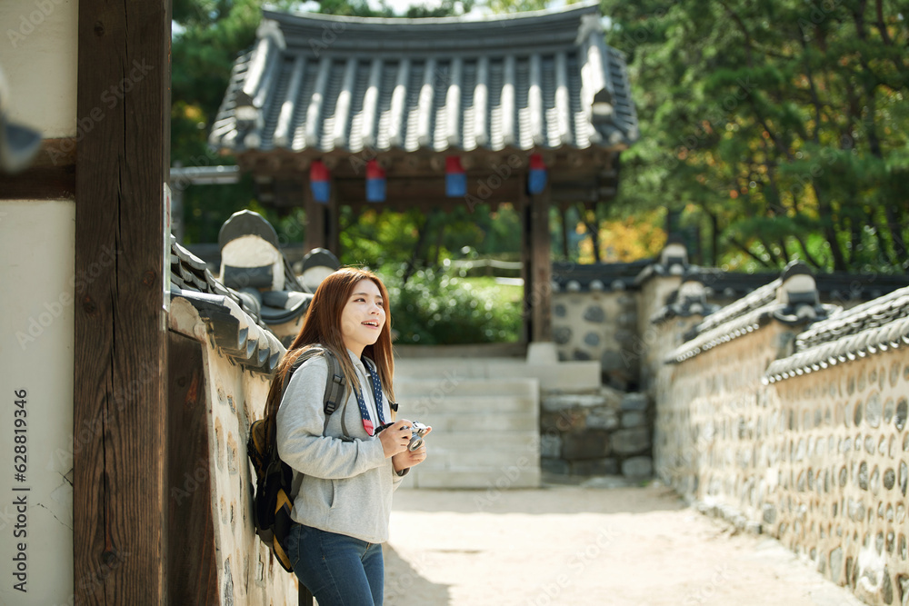 A young woman wearing a camera and taking pictures while traveling to tourist attractions with traditional Korean houses A young woman wearing a camera and taking pictures while traveling to tourist attractions with traditional Korean houses