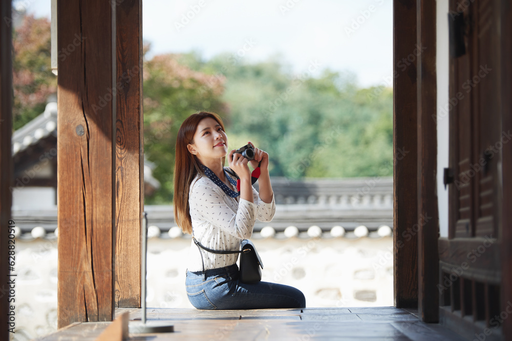 Fototapeta premium A young woman wearing a camera and taking pictures while traveling to tourist attractions with traditional Korean houses