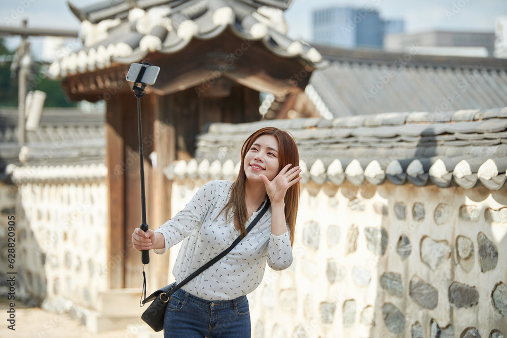 Fototapeta premium A young woman who is taking pictures with a smartphone camera while traveling in a traditional Korean village